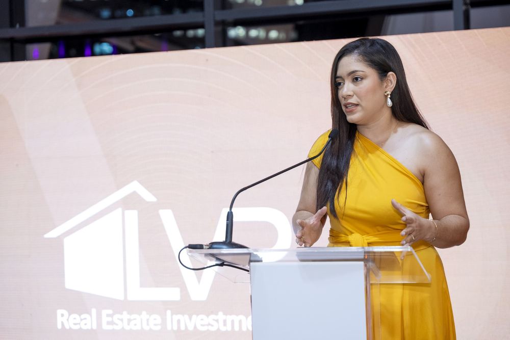 Presentadora en vestido amarillo hablando en el podio del lanzamiento Altos del Este.