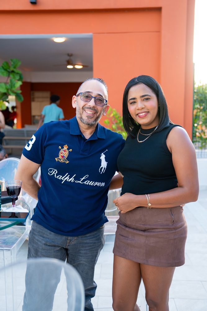 Pareja de invitados sonrie en la terraza de muro naranja del club.