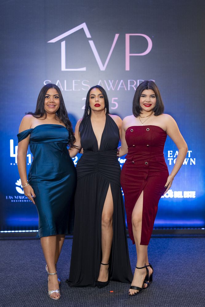 Tres invitadas en vestido de gala posan ante el backdrop de LVP Sales Awards.