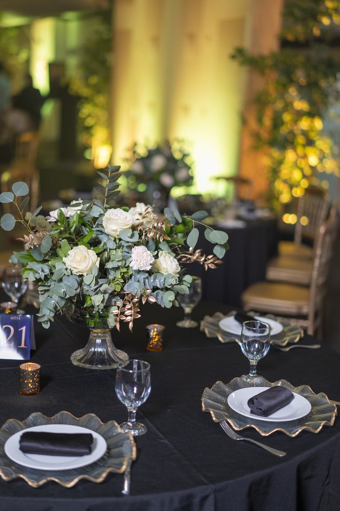 Centro de mesa con rosas blancas y eucalipto sobre el mantel negro.