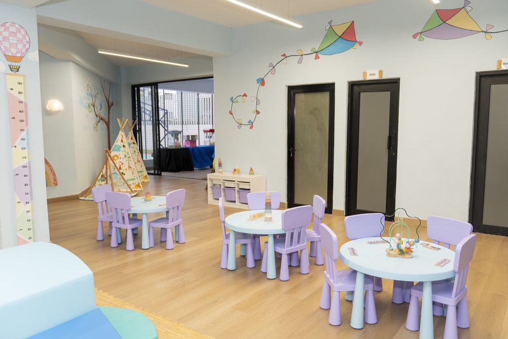 Sala infantil del residencial con mobiliario lila y mural de arcoiris.