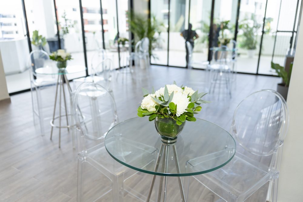 Mesa alta con arreglo de rosas blancas ante el ventanal del salon de ventas.