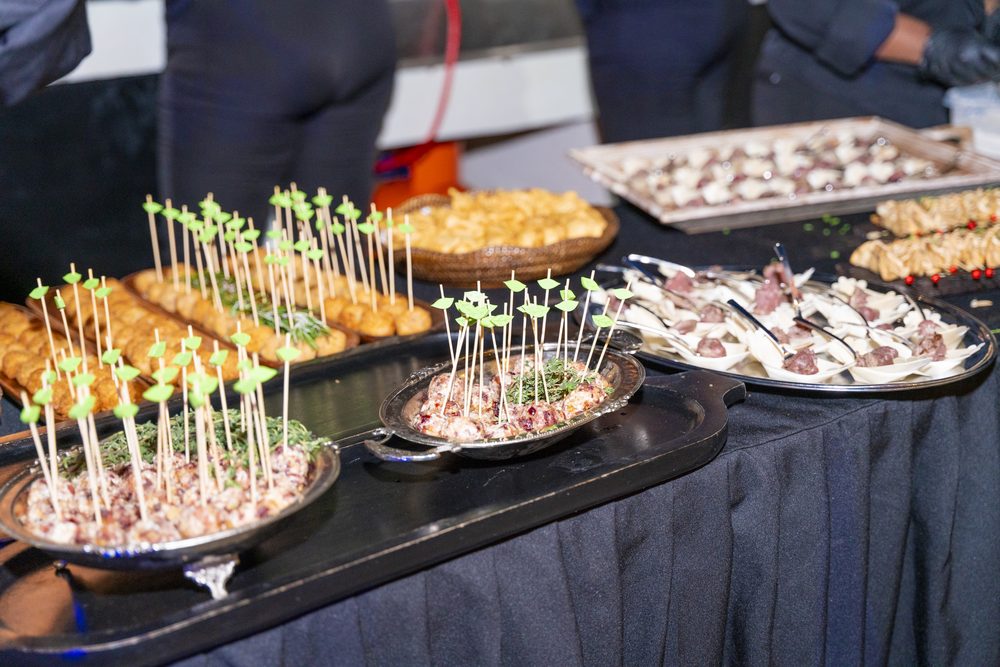 Mesa de catering con bocados servidos en bandejas y brochetas decorativas.