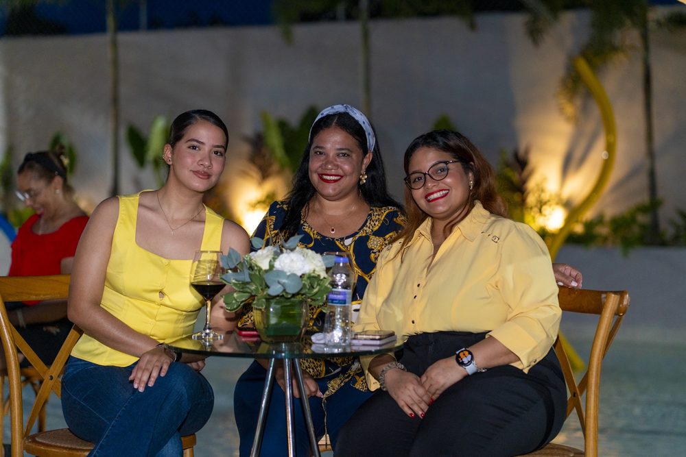 Tres invitadas sonrien en una mesa alta con arreglo floral.