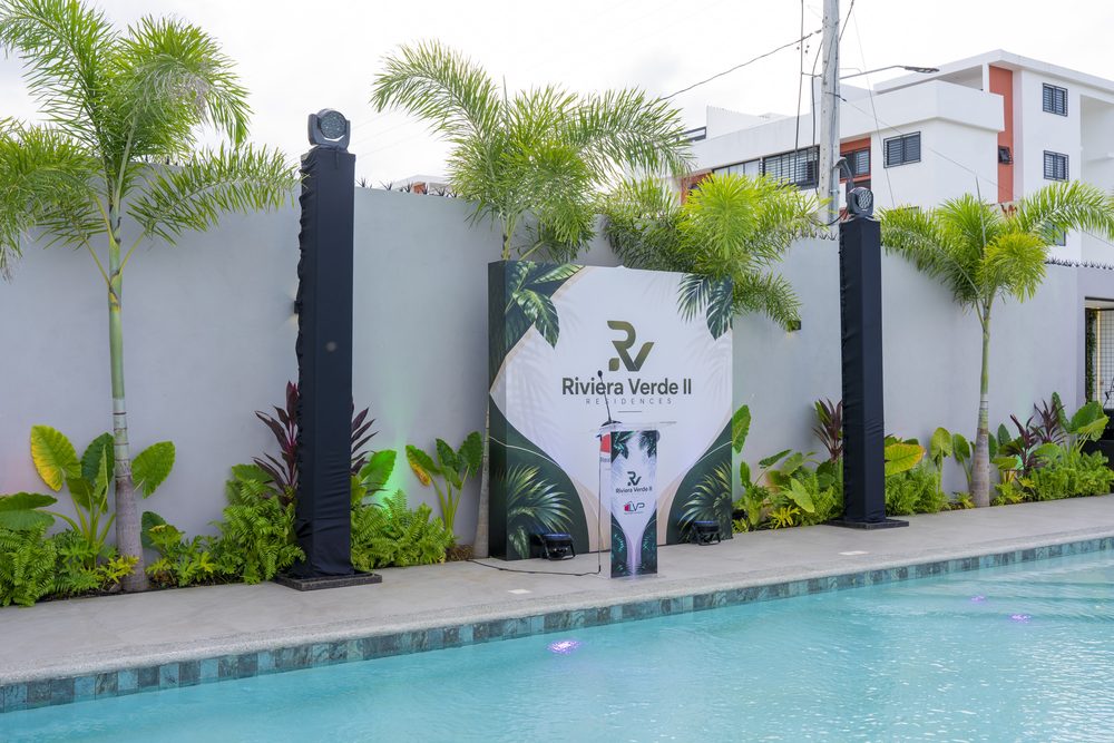 Totem con la marca Riviera Verde II junto a la piscina y la vegetacion tropical.
